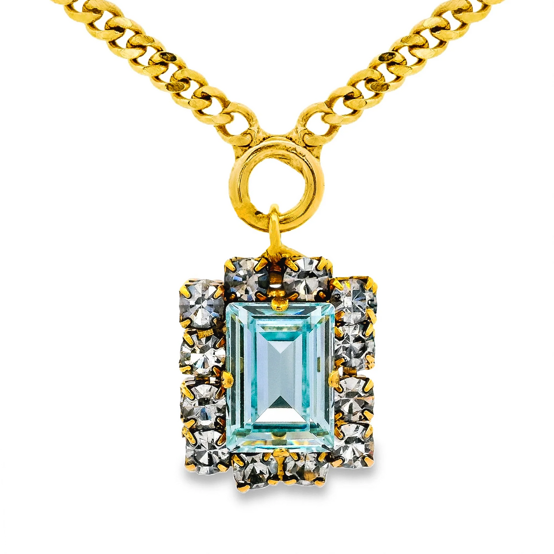 Large blue crystal with clear crystal halo around on gold necklace on plain background