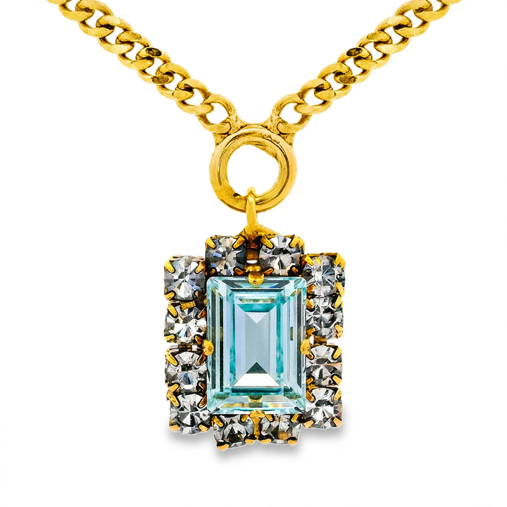 Large blue crystal with clear crystal halo around on gold necklace on plain background