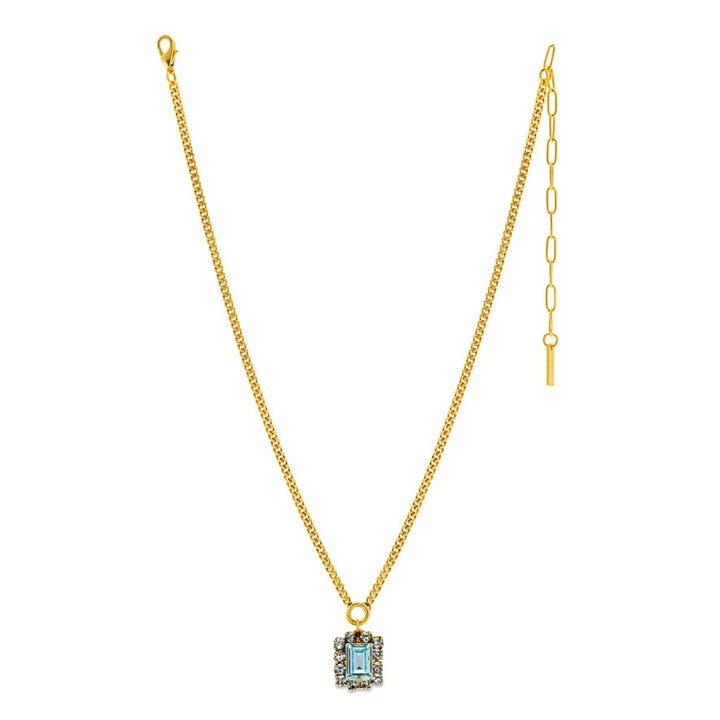 Large blue crystal with clear crystal halo on gold necklace on plain background