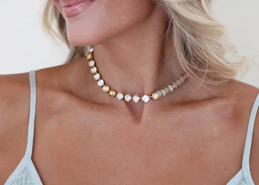 Woman wearing necklace with crystals and stones along with gold spacers on plain background