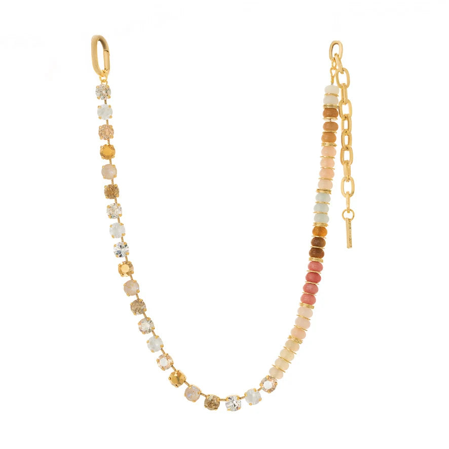 Single gold necklace with multi color crystals and stones along with gold spacers on plain background