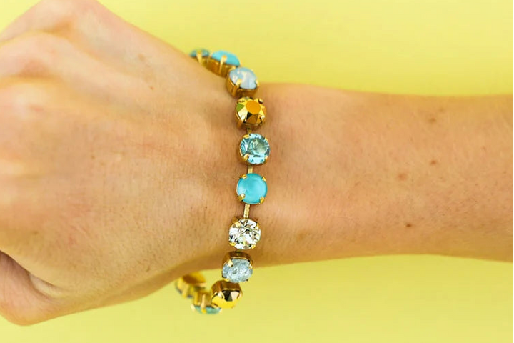 Arm wearing multi color blue Swarovski Crystal bracelet on plain background