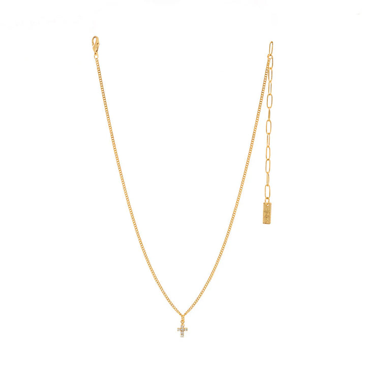 A delicate gold chain necklace featuring a small cross pendant and an adjustable paperclip extender with a rectangular tag, displayed on a solid white background.