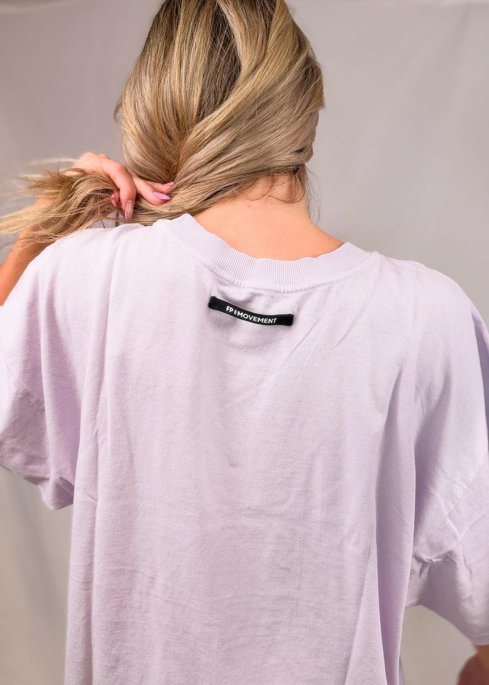 Woman shown from back wearing purple tee with 'FP MOVEMENT' branding on top on plain background