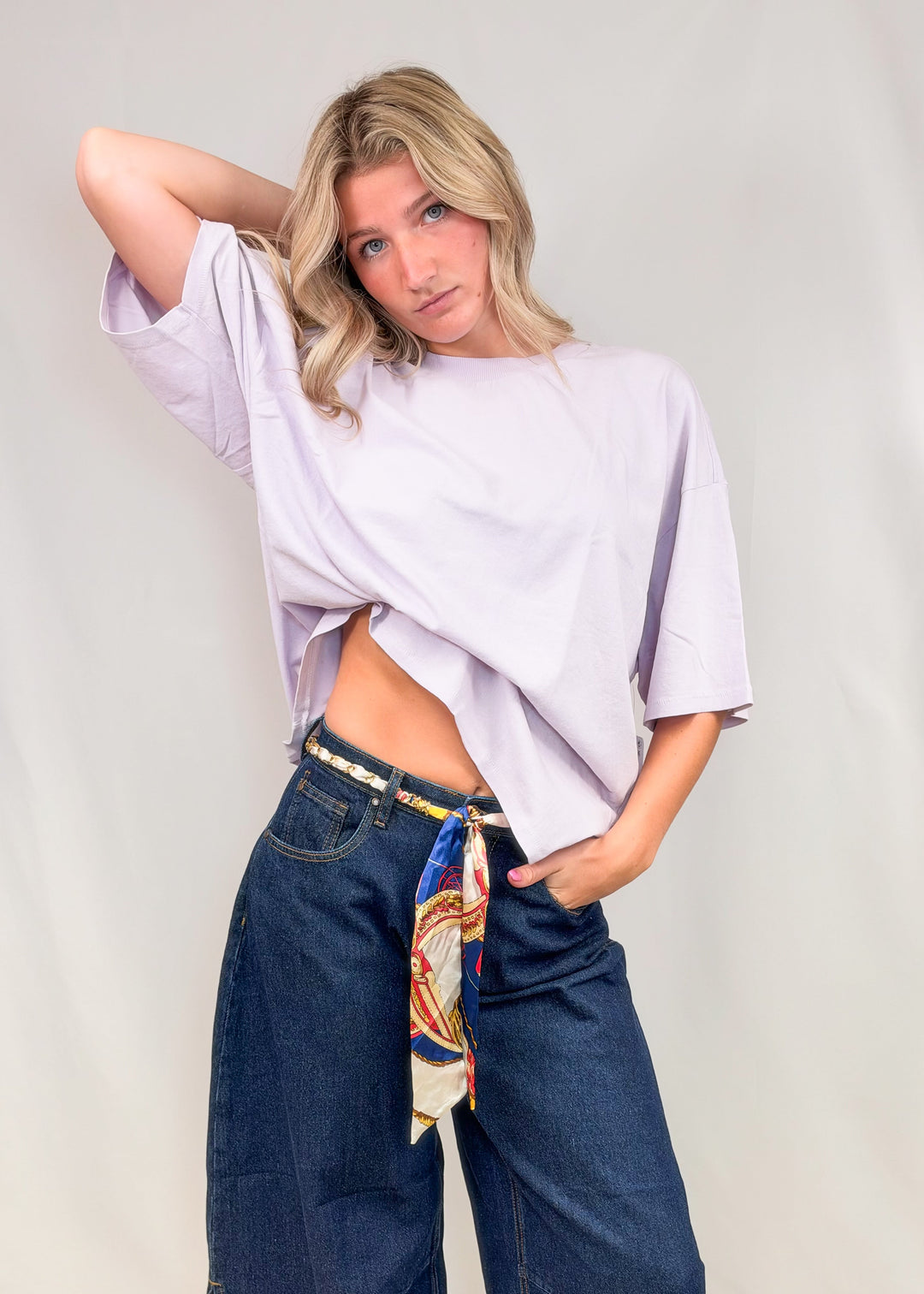 Woman wearing purple tee with dark denim jeans on plain background