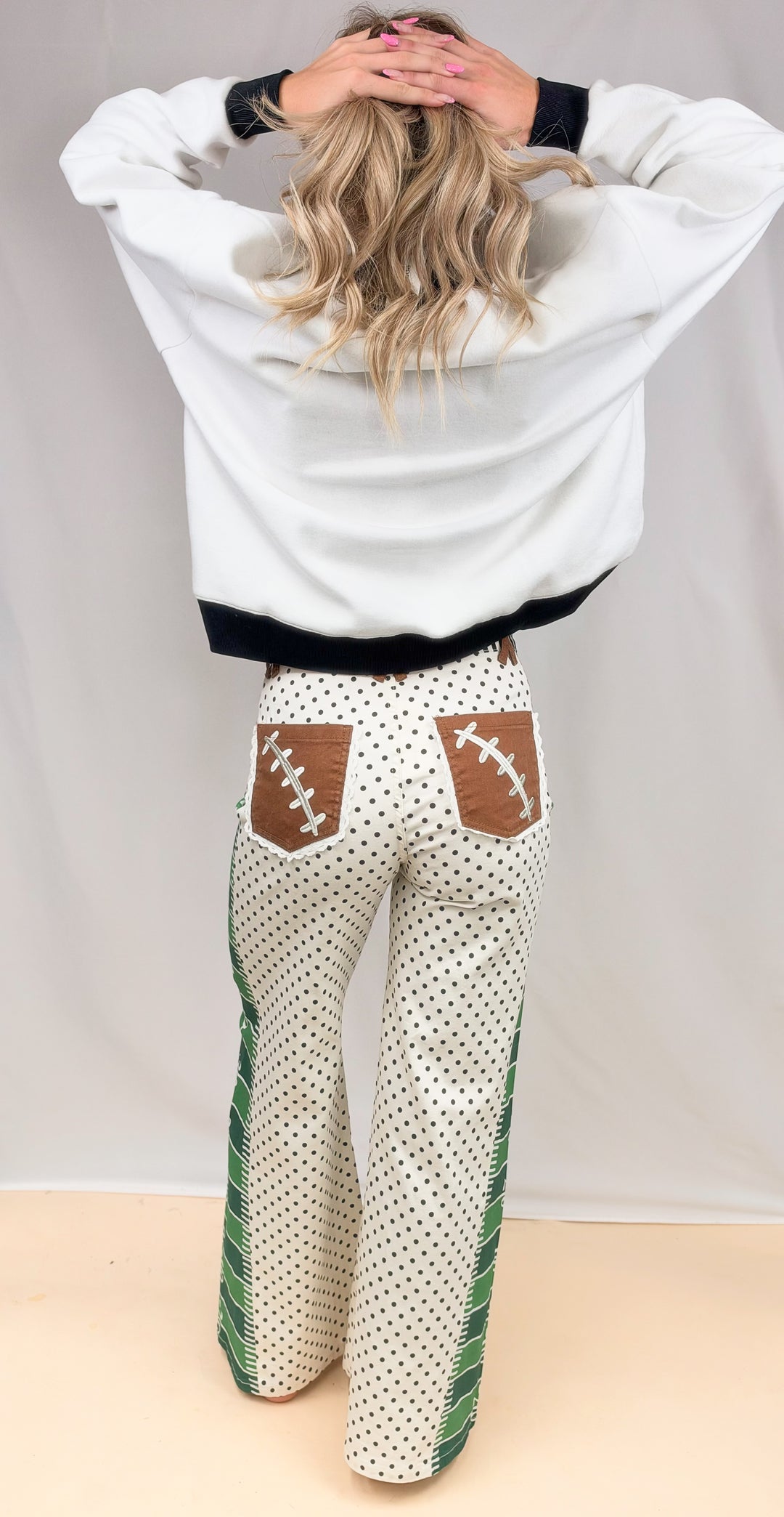 Woman shown from back wearing black and white mock neck and football detail pants on plain background