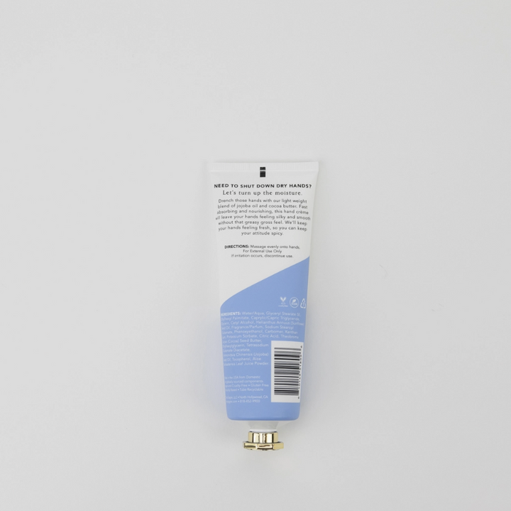 The back of a white and light blue squeeze tube of toothpaste is shown against a light gray background, with a small gold cap placed below it.