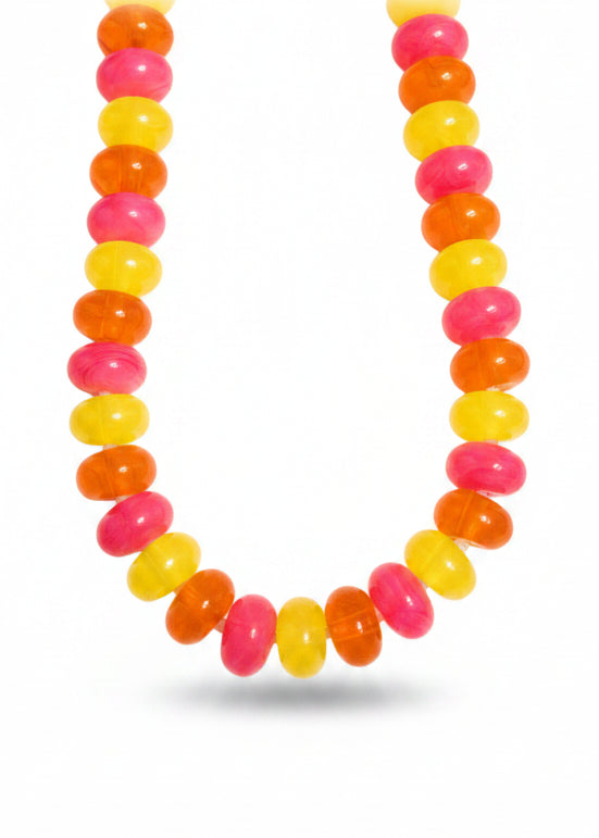 A beaded necklace made of translucent round beads in alternating bright pink, orange, and yellow, photographed on a white sheet of paper.