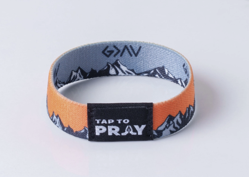 A fabric wristband with an orange outer band, a gray inner band with a black mountain pattern, and a black center tab that reads &