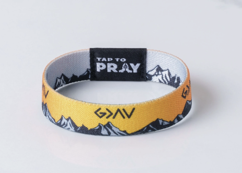 A fabric wristband with a yellow outer band featuring a black and white mountain pattern and the word &