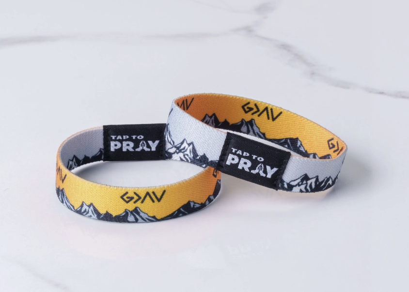 Two fabric wristbands with a yellow, white, and black mountain pattern and black text reading &