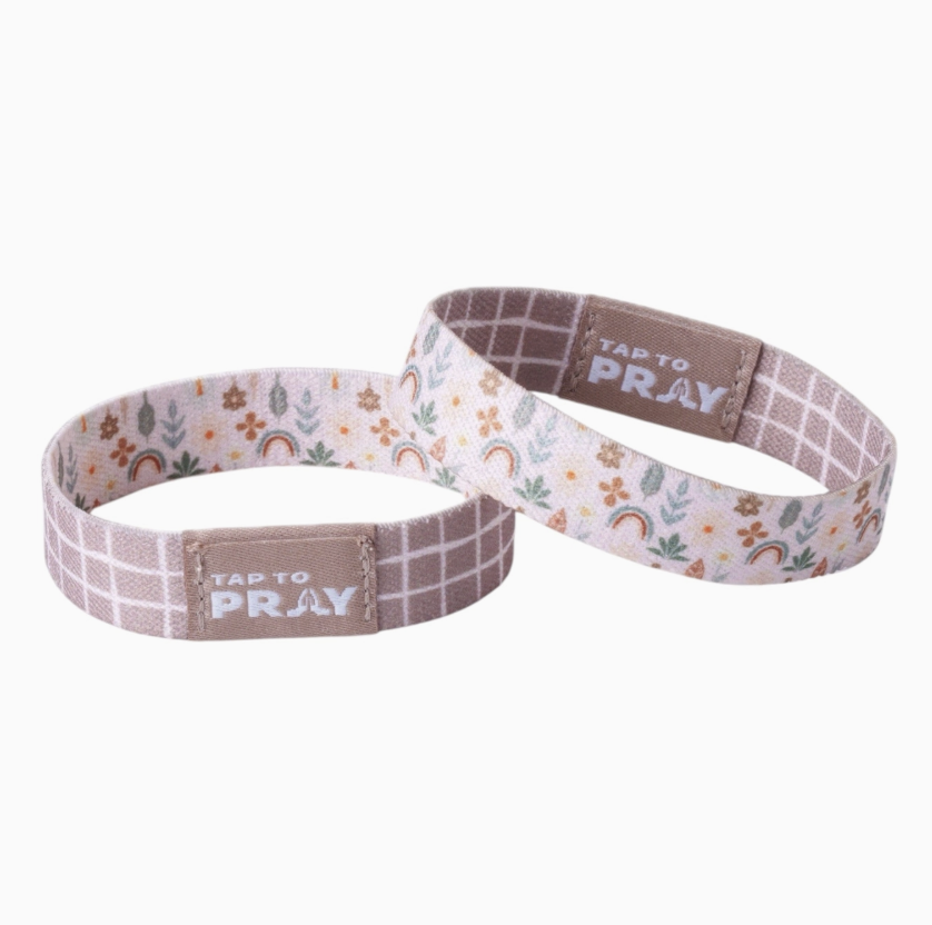 Two fabric wristbands with a floral and rainbow pattern on a white background, featuring a brown tab with the text 'TAP TO PRAY'.