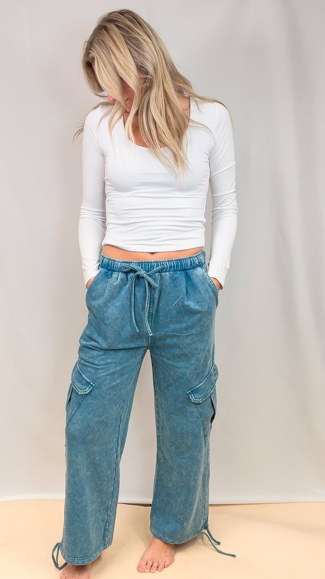 Woman wearing white top and teal blue pants on plain background