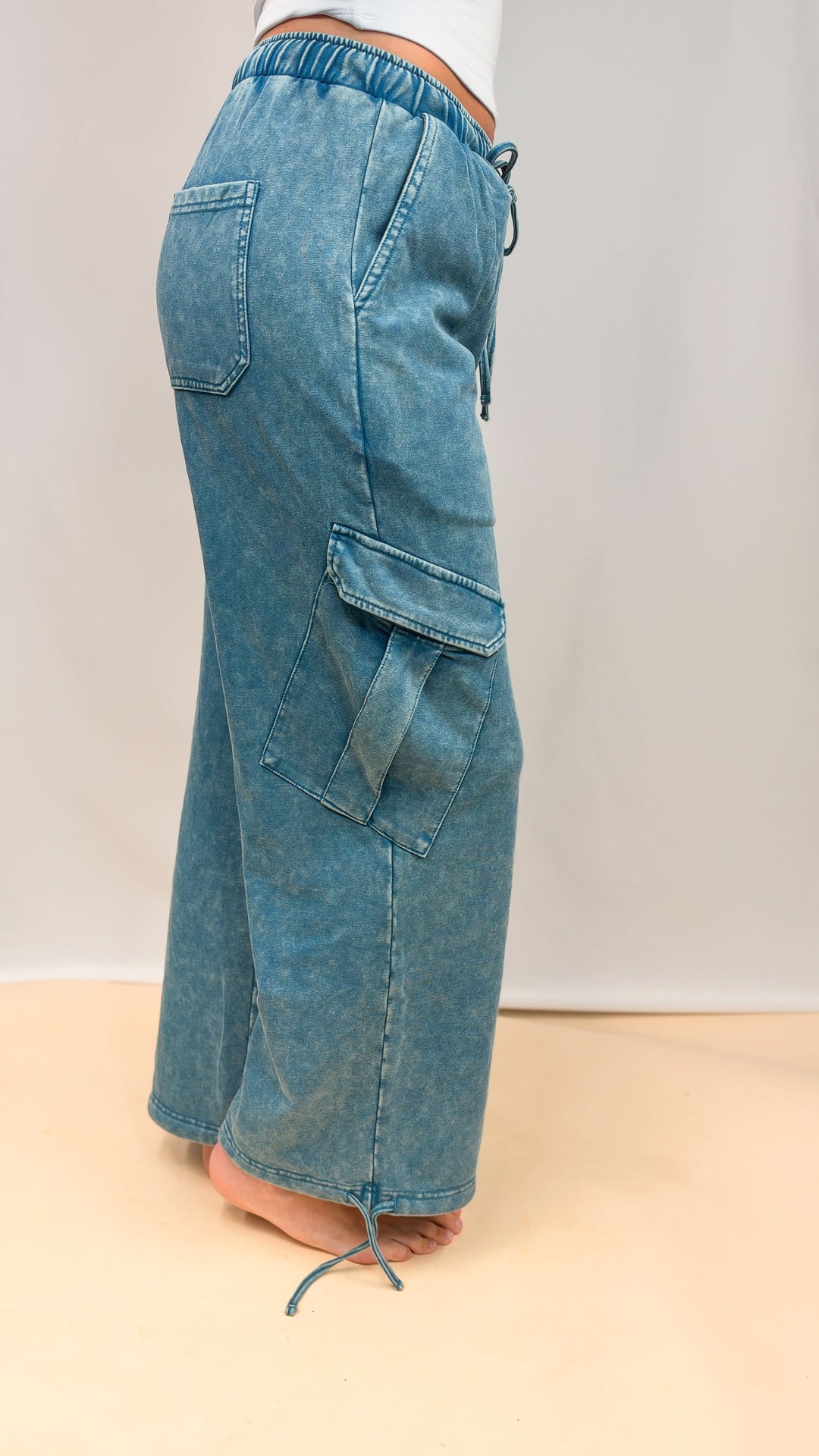 Woman shown from side view wearing teal blue pants on plain background