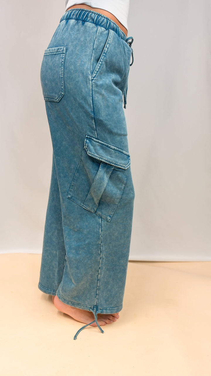 Woman shown from side view wearing teal blue pants on plain background