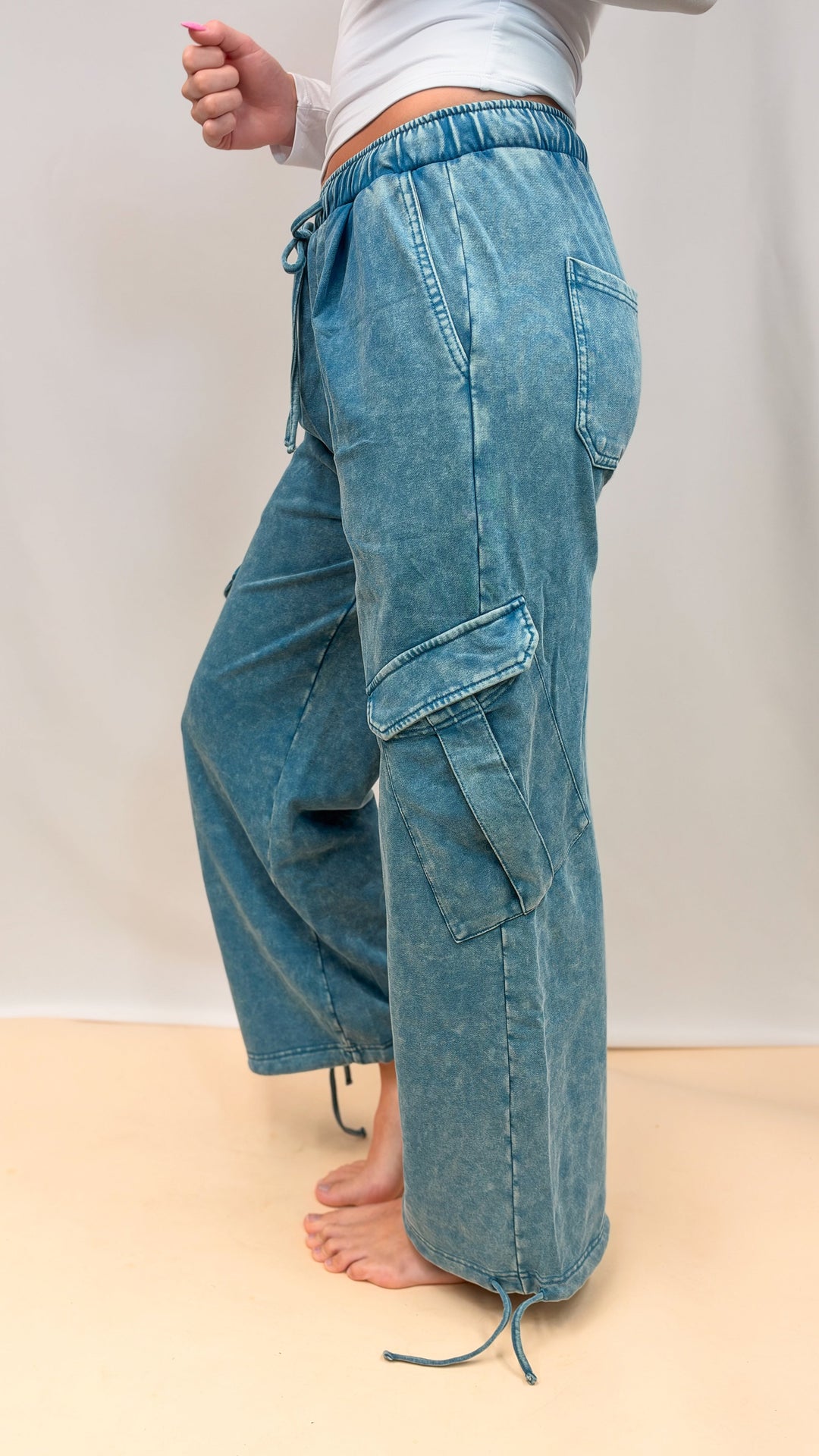 Woman shown from side view wearing teal blue pants on plain background