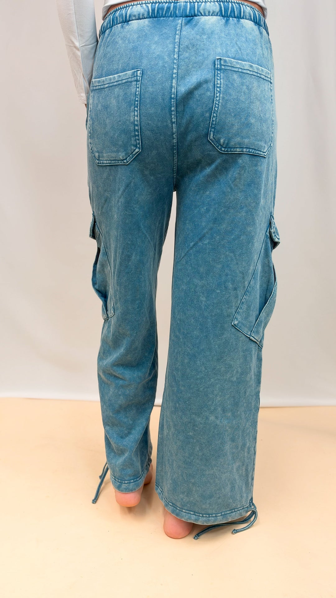 Woman shown from back view wearing teal blue pants on plain background
