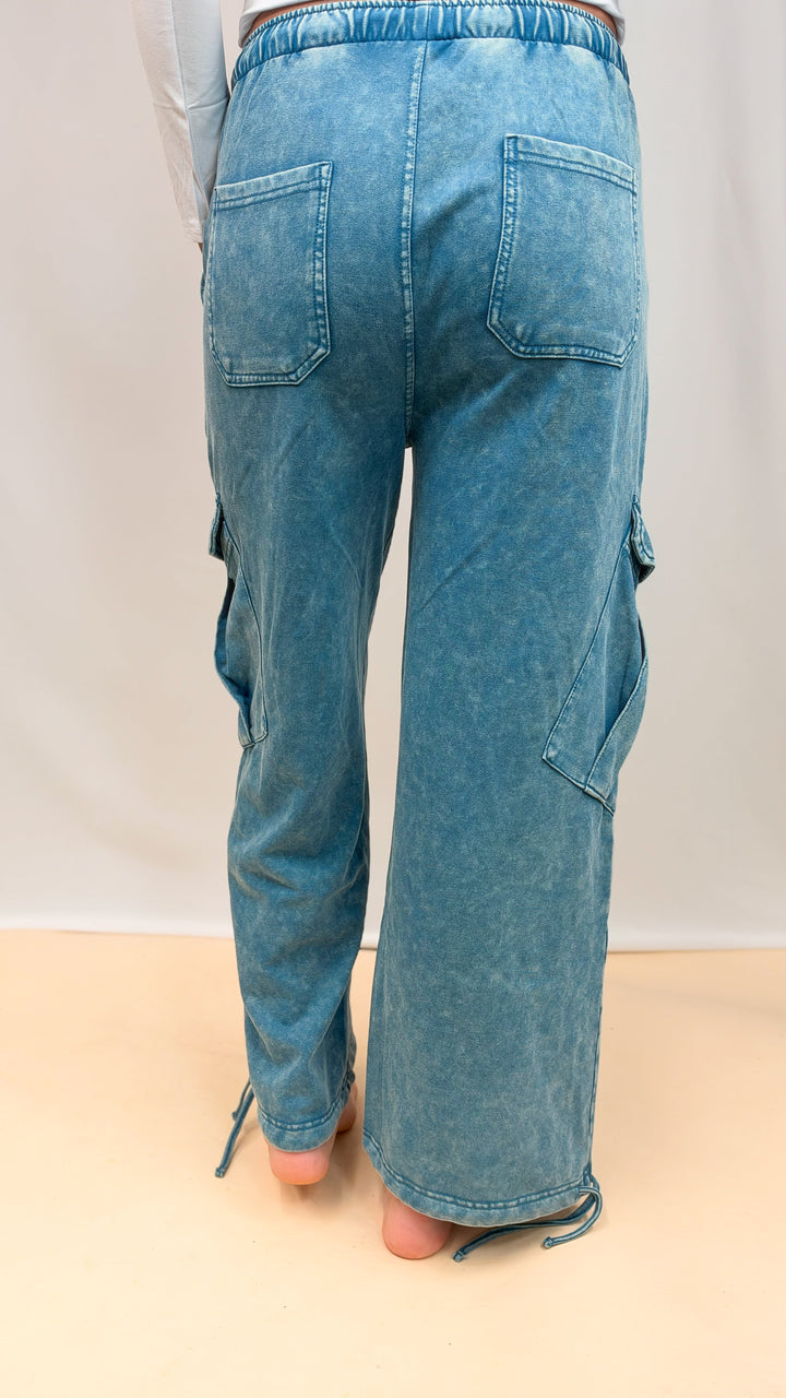 Woman shown from back view wearing teal blue pants on plain background