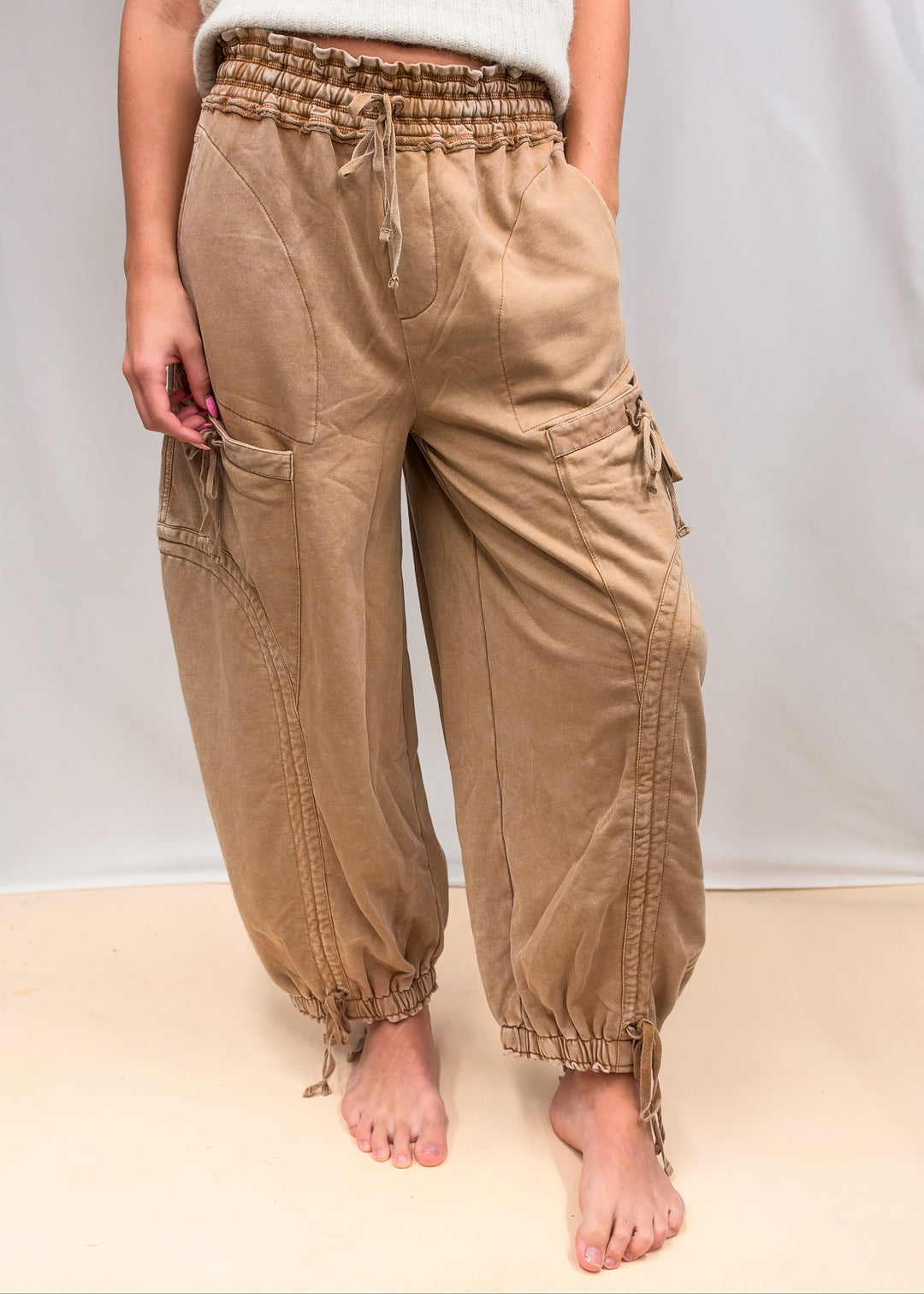 Woman wearing camel color pants with drawstring details and beige top on plain background