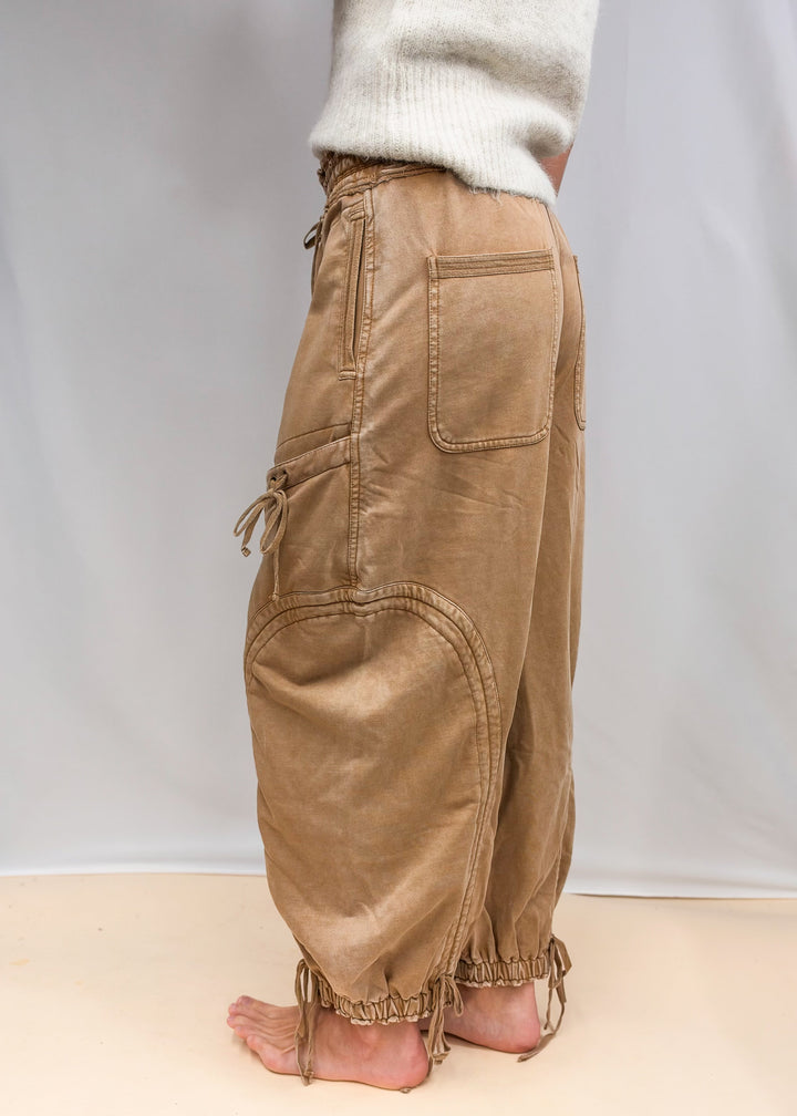 Woman wearing camel color sweatpants with drawstring details and cream top on plain background