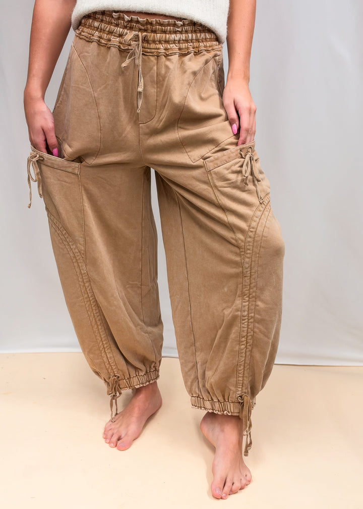 Woman wearing camel color sweatpants with drawstring details and cream top on plain background