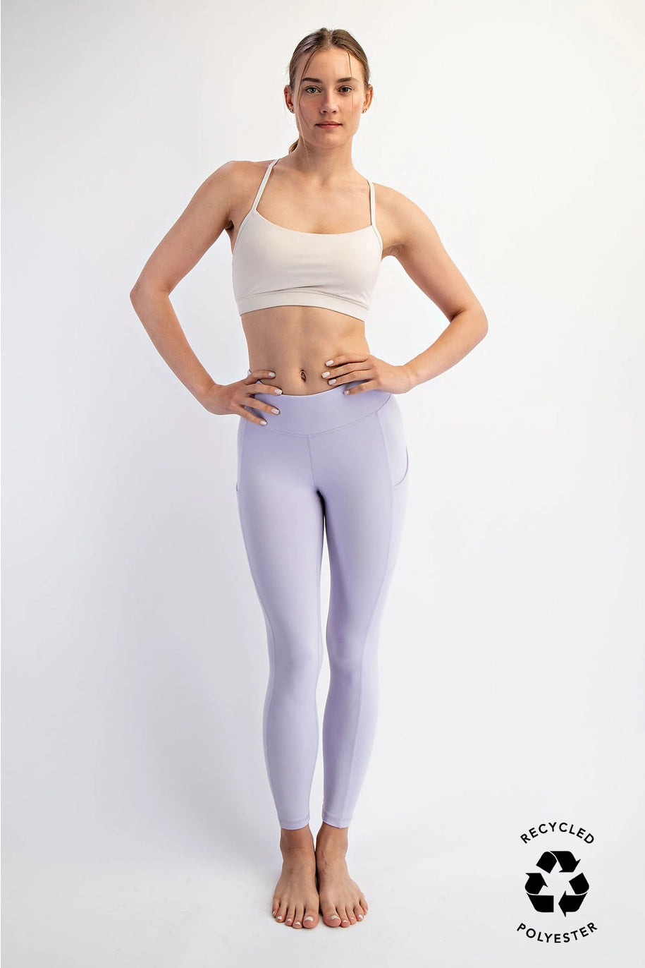 woman wearing purple leggings and white sports bra on plain background