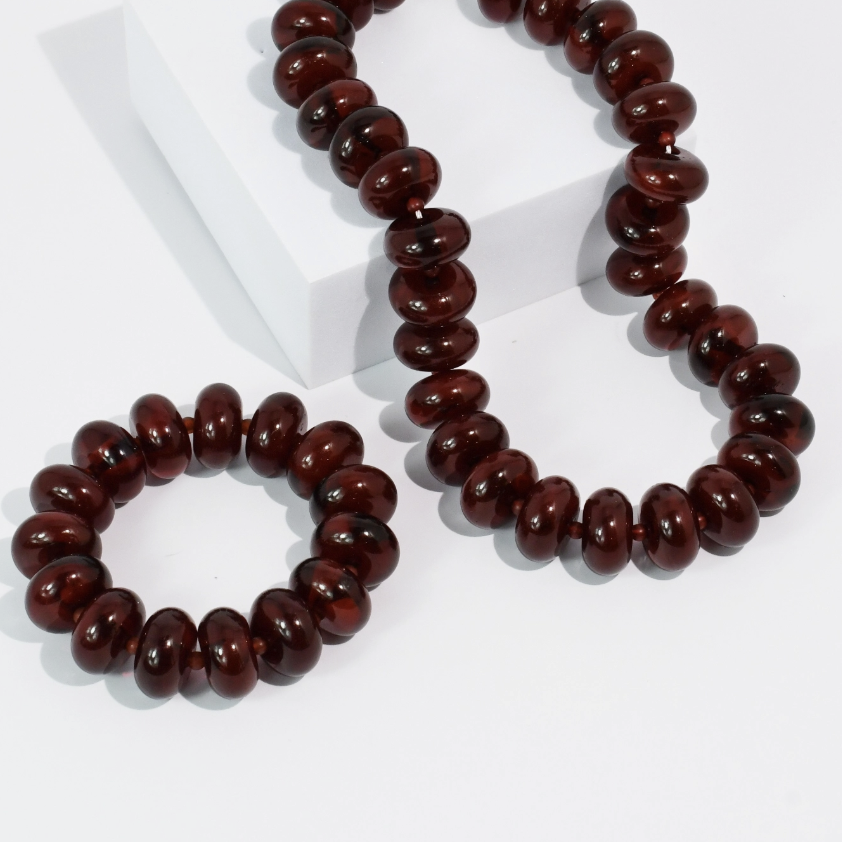 A dark reddish-brown beaded necklace and matching beaded bracelet displayed on a clean white background with a white geometric block.