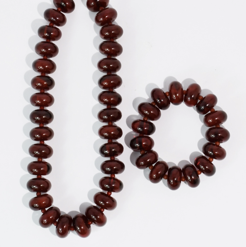 A dark reddish-brown beaded necklace and matching beaded bracelet made of glossy, rounded disc-like beads, displayed on a clean white background.