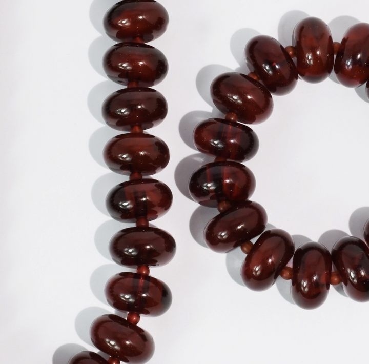 Dark reddish-brown glossy oval beads strung on cords, arranged on a white background.