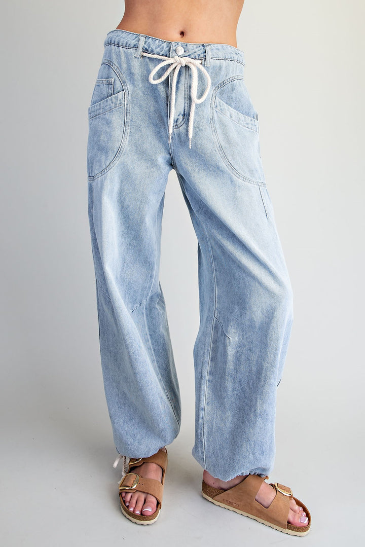 Light wash wide-leg denim jeans with a white drawstring waist, shown on a model from the waist down wearing brown slide sandals against a light gray studio background.