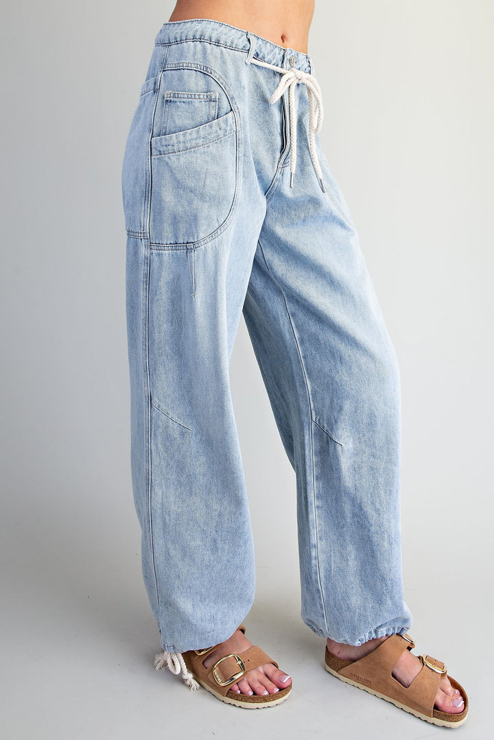 Light wash blue denim wide-leg pants with an elastic drawstring waist and cuffed ankles, shown on a model wearing brown slide sandals against a light gray studio background.