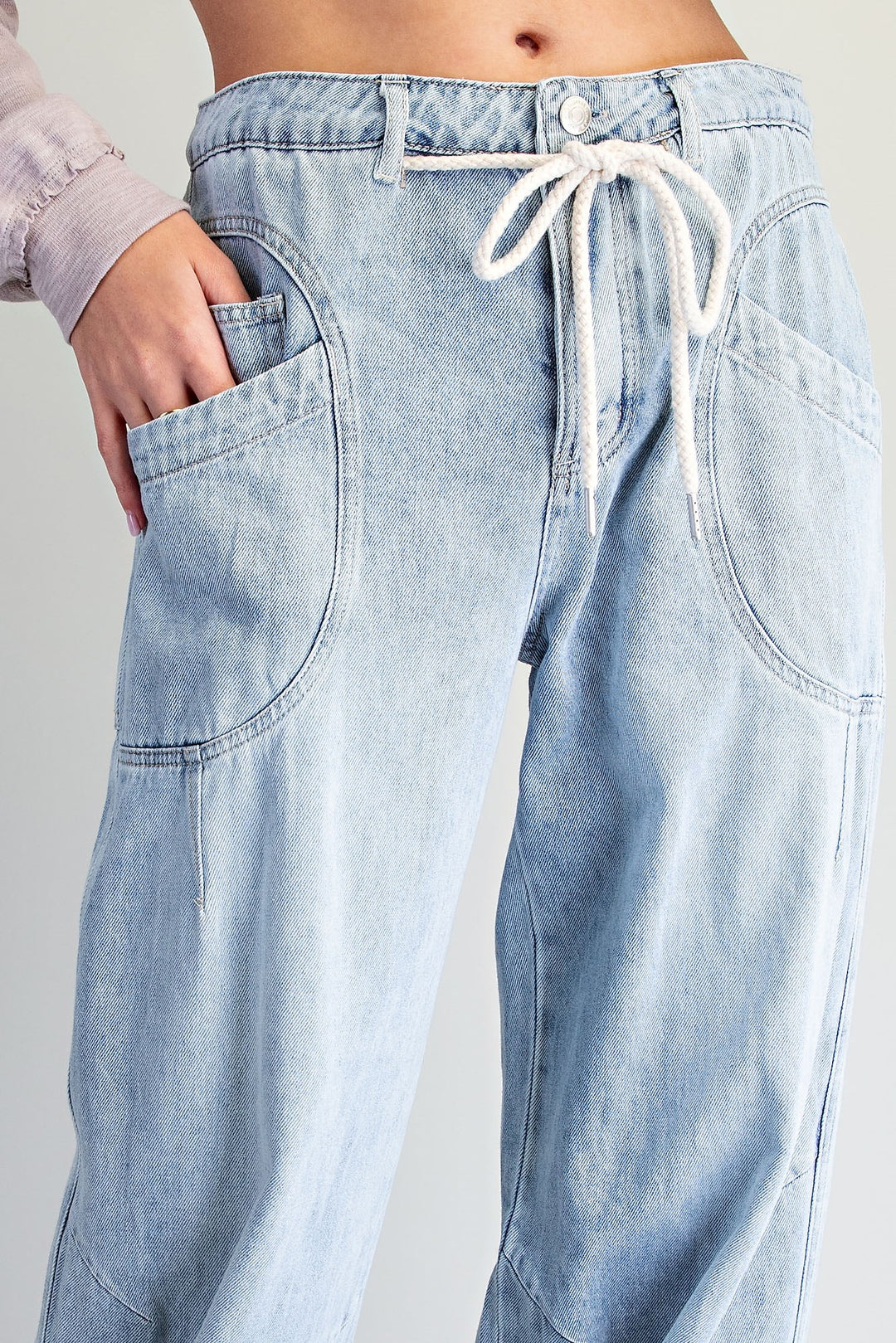 Close-up of a person wearing light-wash blue denim pants with a white drawstring waist, side pockets, and a relaxed straight-leg fit.