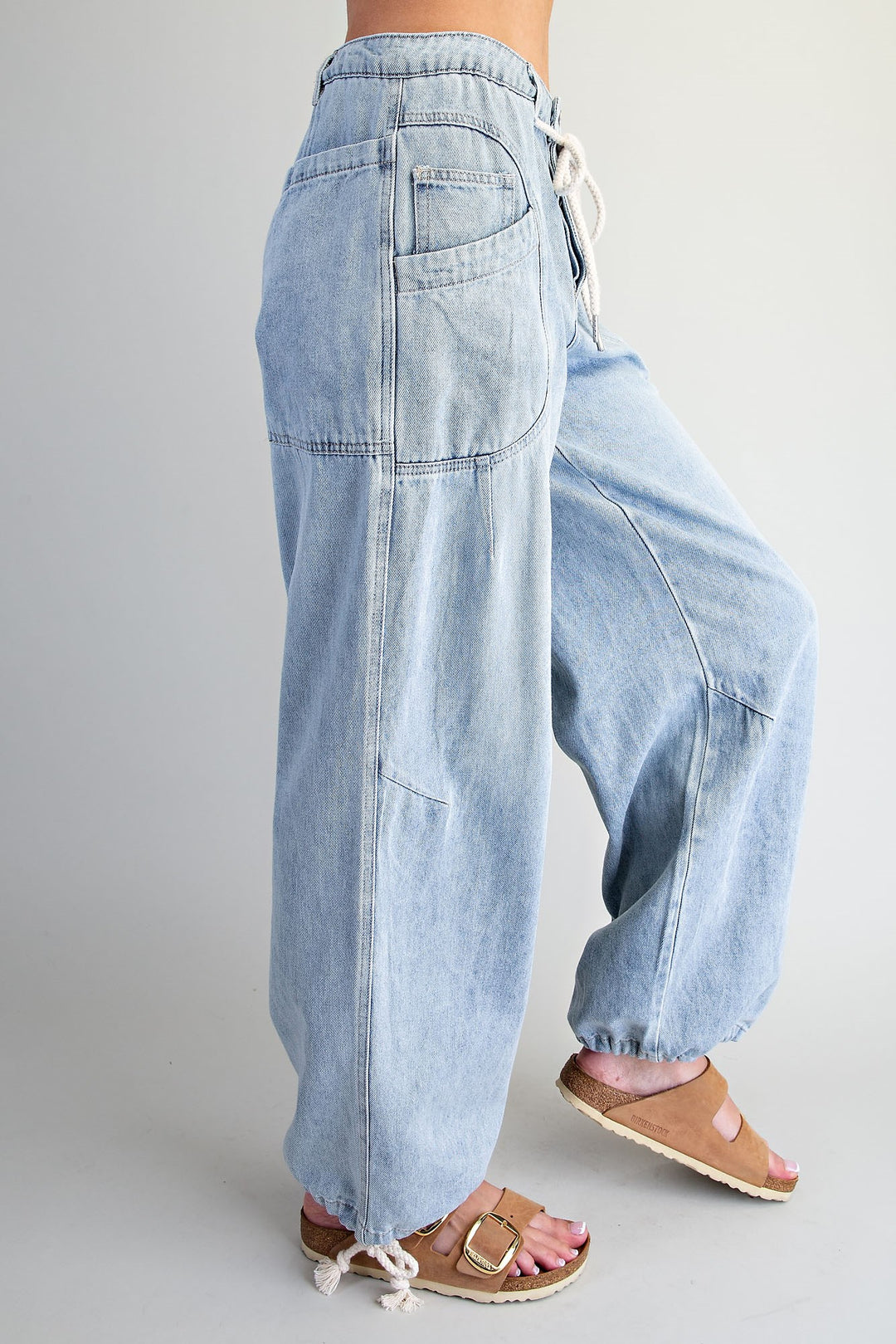 Light wash blue denim wide-leg pants with a drawstring waist and cuffed ankles, shown on a model from the side against a light gray studio background.