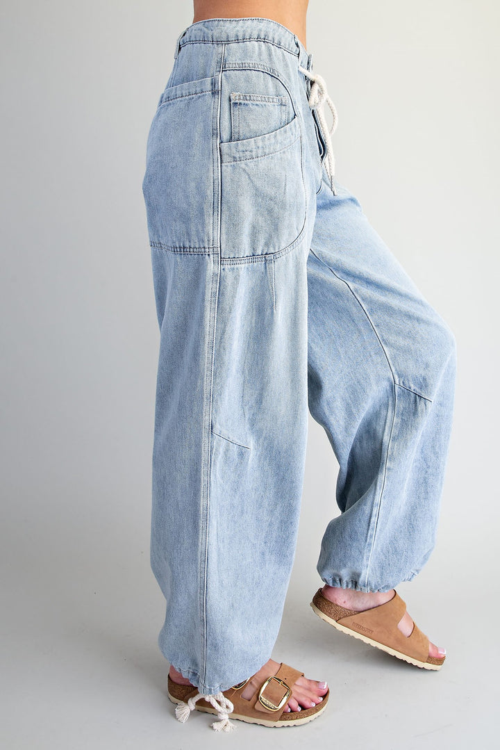 Light wash blue denim wide-leg pants with a drawstring waist and cuffed ankles, shown on a model from the side against a light gray studio background.