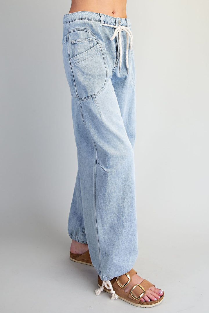 Light wash blue denim wide-leg pants with an elastic drawstring waist and side pockets, shown on a model from the waist down wearing brown sandals against a light gray studio background.