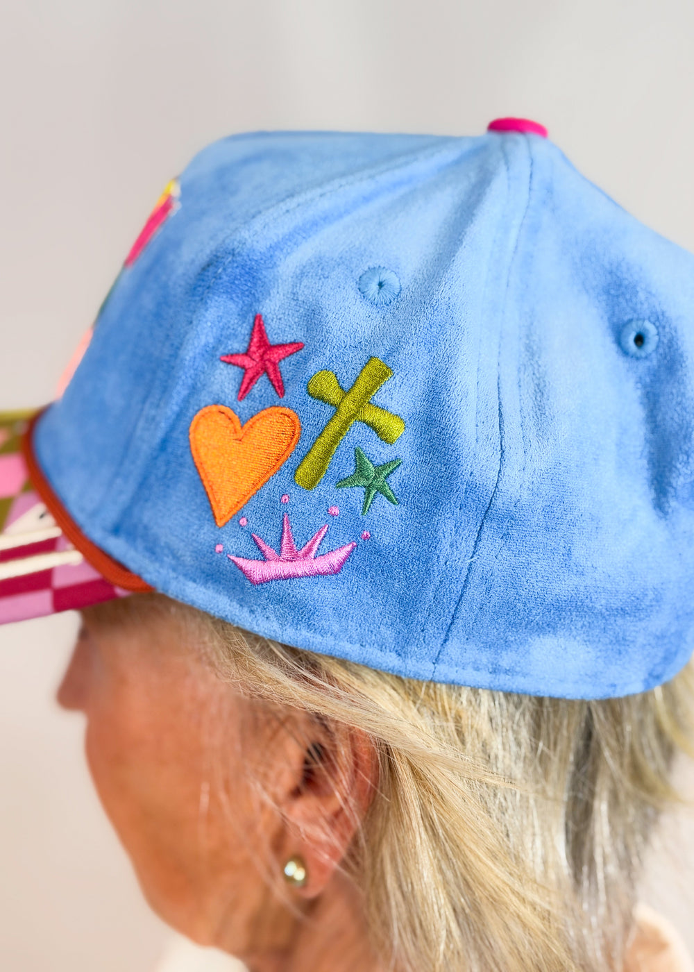 Woman shown from side wearing blue suede hat with embroidery designs on plain background