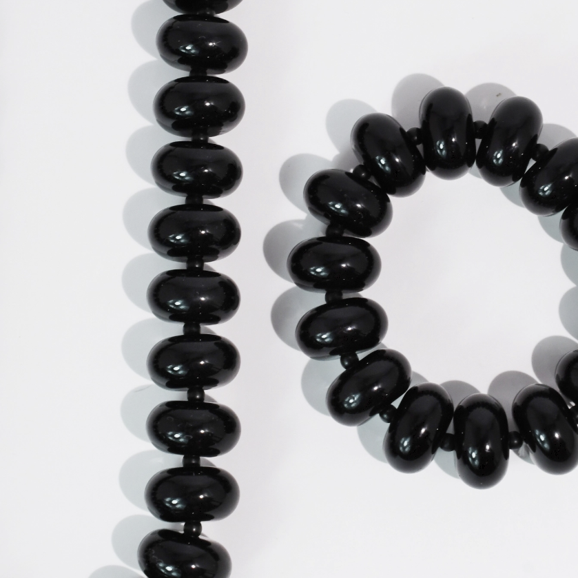 Black glossy oval beads arranged in a long strand and a bracelet on a white background.