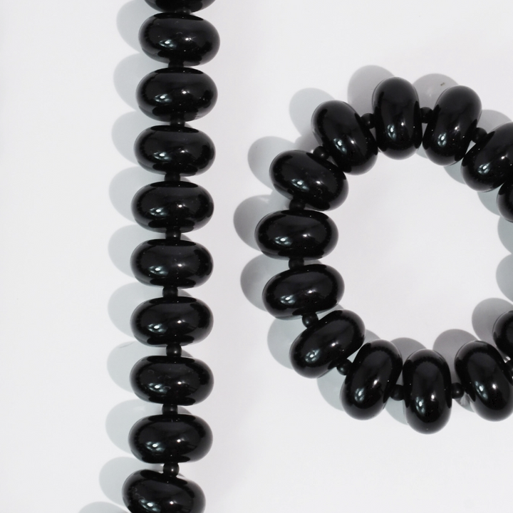 Black glossy oval beads arranged in a long strand and a bracelet on a white background.