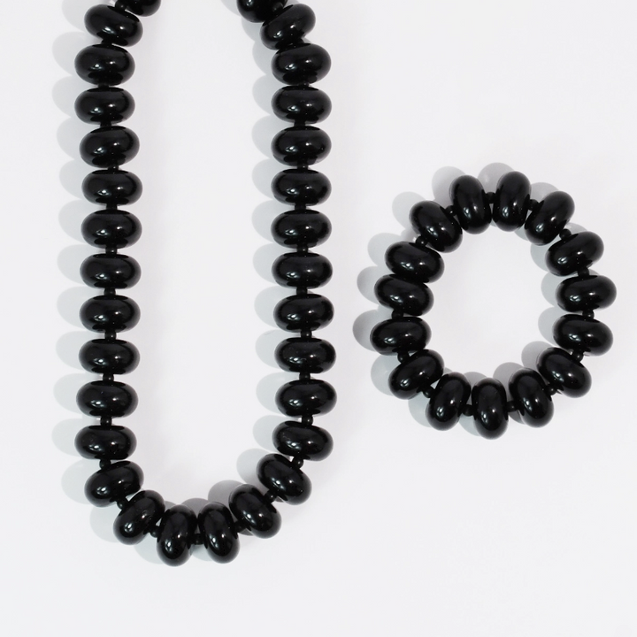 A black beaded necklace and matching beaded bracelet made of glossy, rounded disc-like beads, displayed on a clean white background.