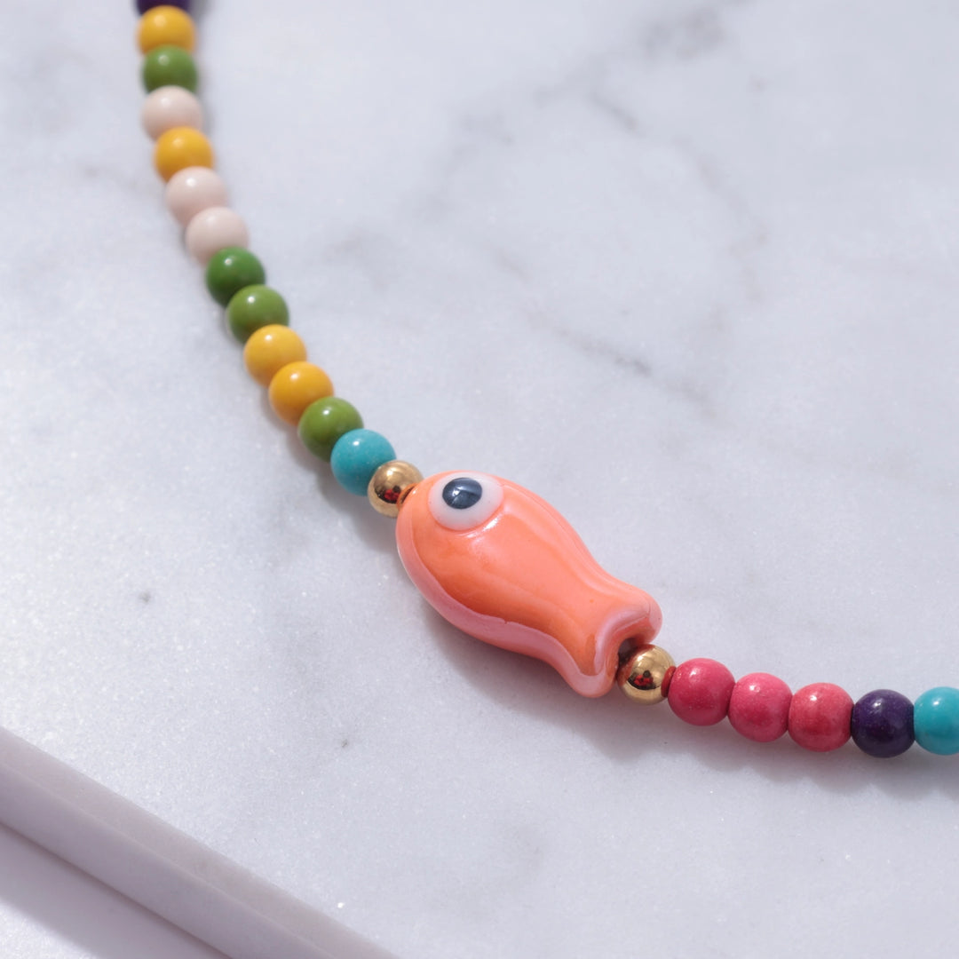 Colorful beaded necklace with a fish-shaped charm on a marble surface