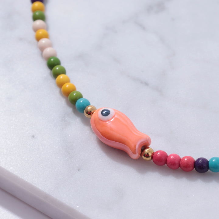 Colorful beaded necklace with a fish-shaped charm on a marble surface