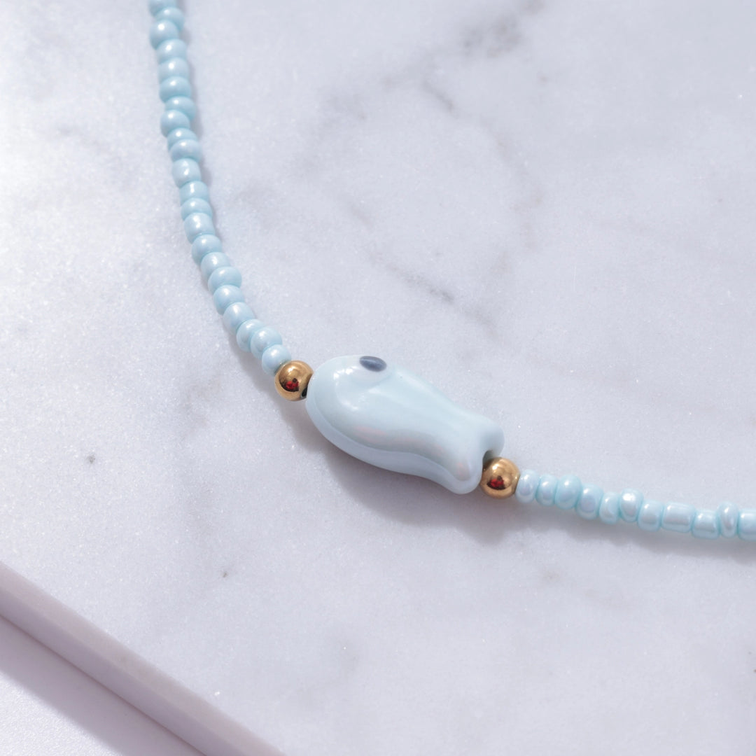 Necklace with a light blue whale pendant on a marble surface