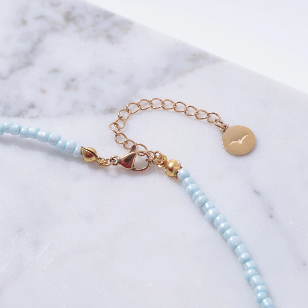 Bracelet with light blue beads and gold accents on a marble surface