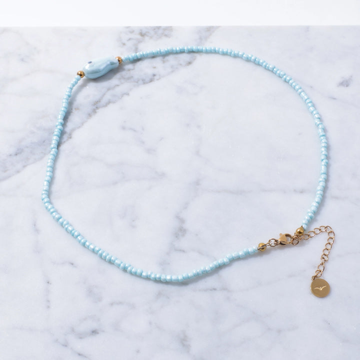 Light blue beaded necklace with gold accents on a marble surface