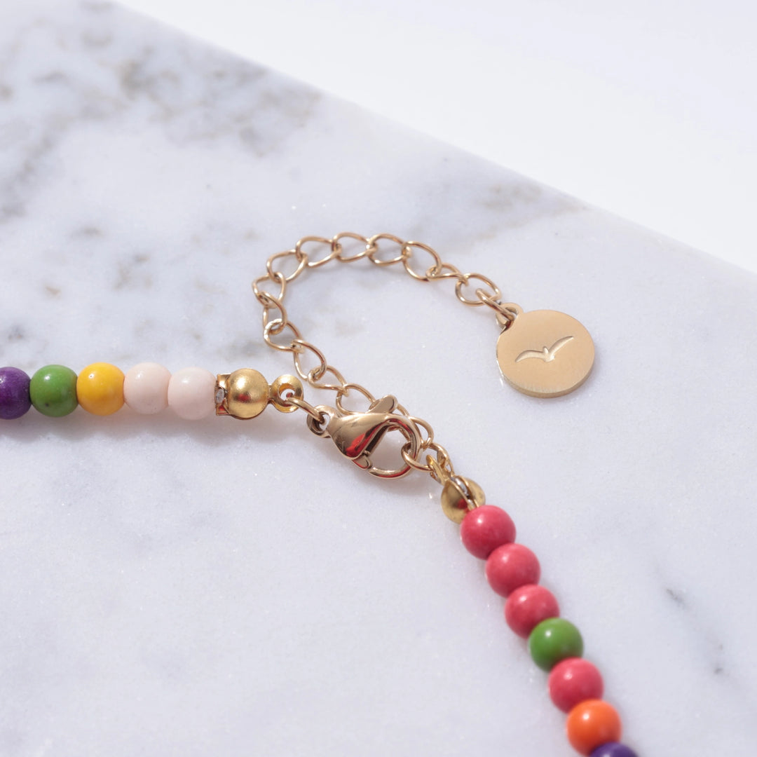 Colorful beaded bracelet with a gold chain on a marble surface