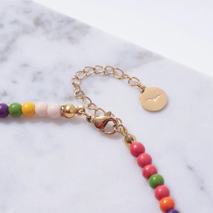 Colorful beaded bracelet with a gold chain on a marble surface
