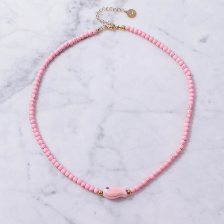 Pink beaded necklace with a pink fish charm on a marble background