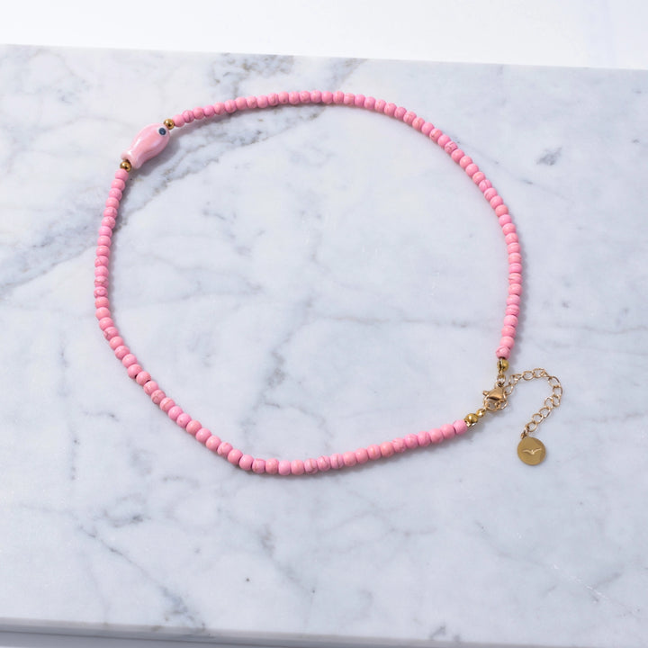 Pink beaded necklace with gold clasp on a marble surface
