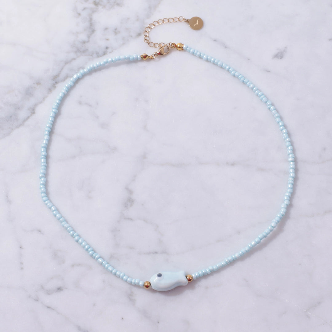 Necklace with light blue beads and a white fish-shaped pendant on a marble surface