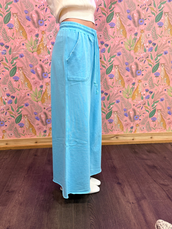 Person wearing light blue pants standing in front of a pink wall with cheetah and floral pattern.